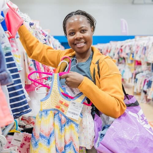 A mom and grandmother stand beside a rack of clothing at a JBF sale in Texas.